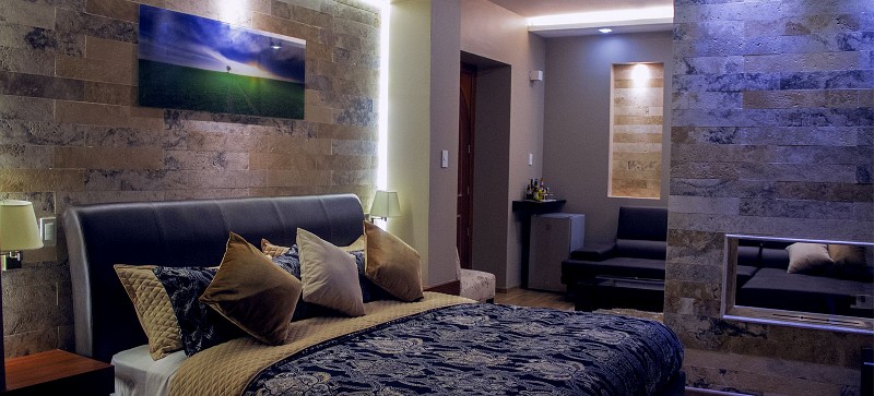Cama grande con pared de piedra iluminada y cuadro