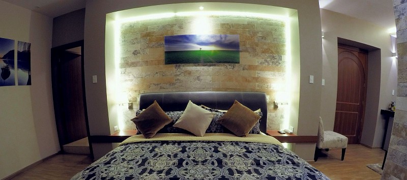 Cama de frente con cabecero de cuero y pared iluminada