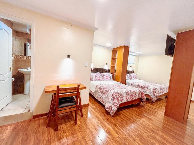 Habitación con dos camas, escritorio y baño privado a la vista