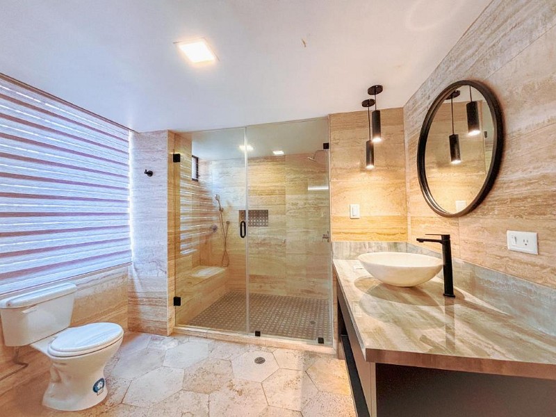 Baño de mármol con ducha grande de vidrio, espejo redondo y lavabo de piedra