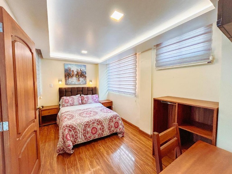 Habitación matrimonial con techo iluminado, dos ventanas y escritorio