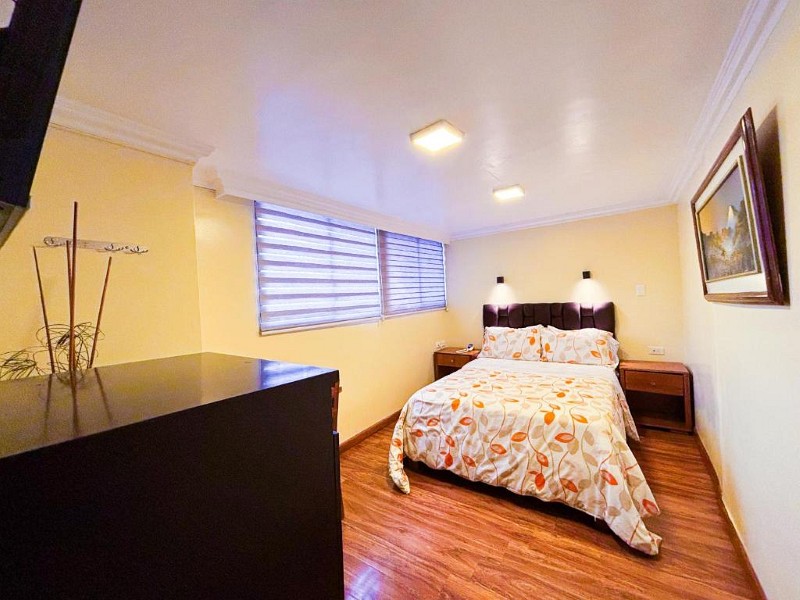 Habitación matrimonial con dos ventanas, mesitas de noche y cuadro